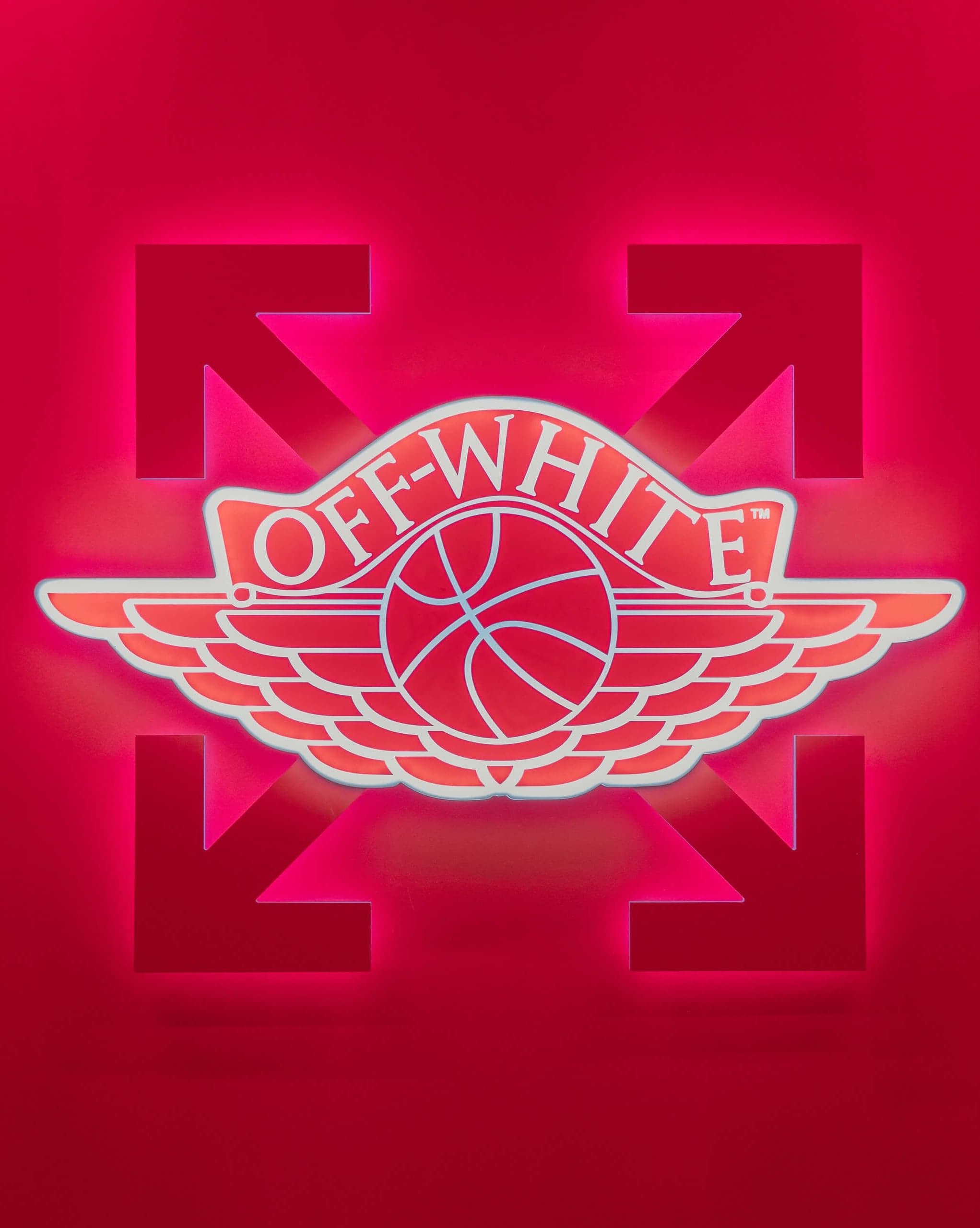 A red Off-White Air Jordan wings logo glowing on a red wall