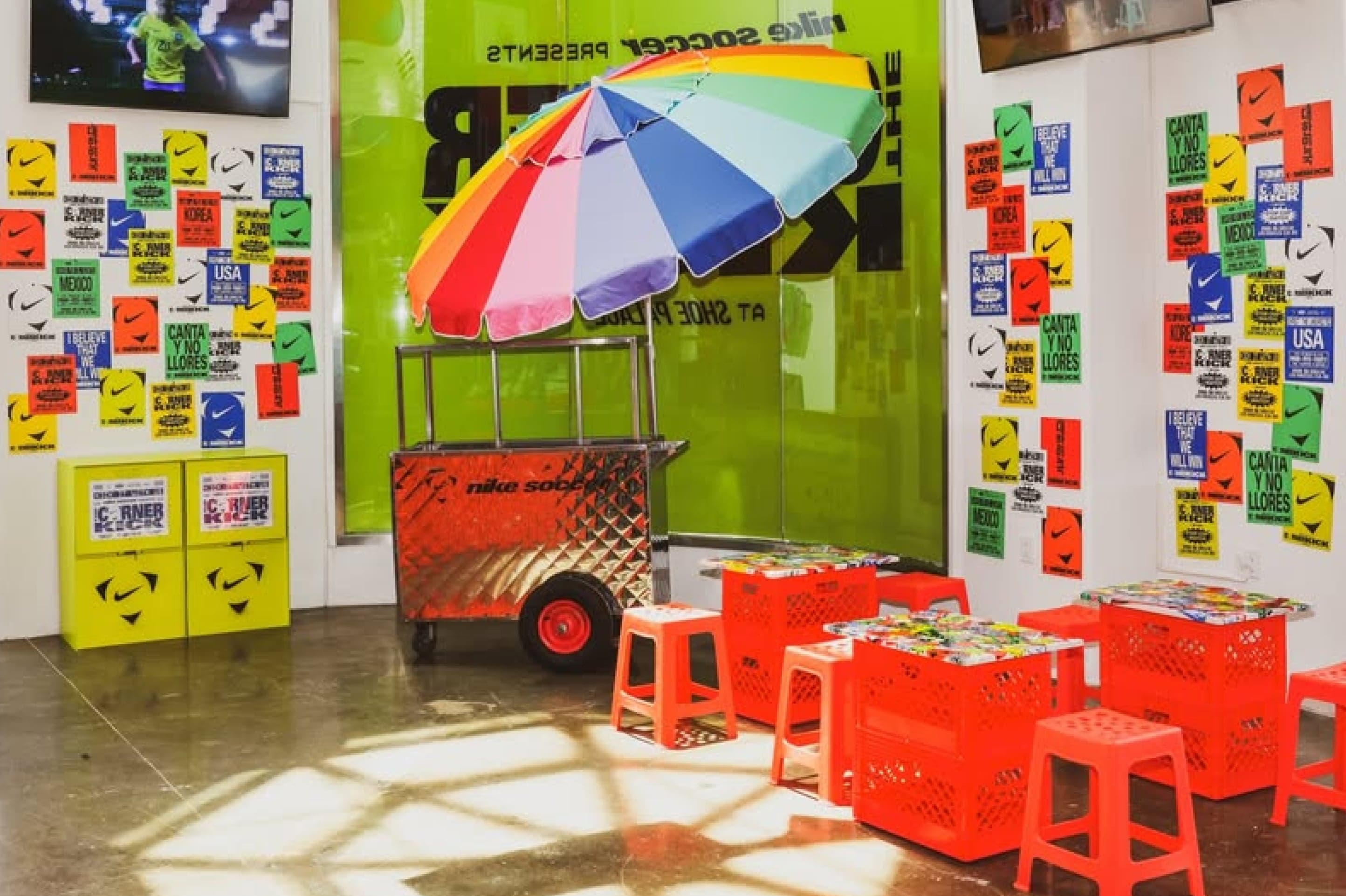 A lounge corner with a striped umbrella and red stools in front of walls of colourful stickers