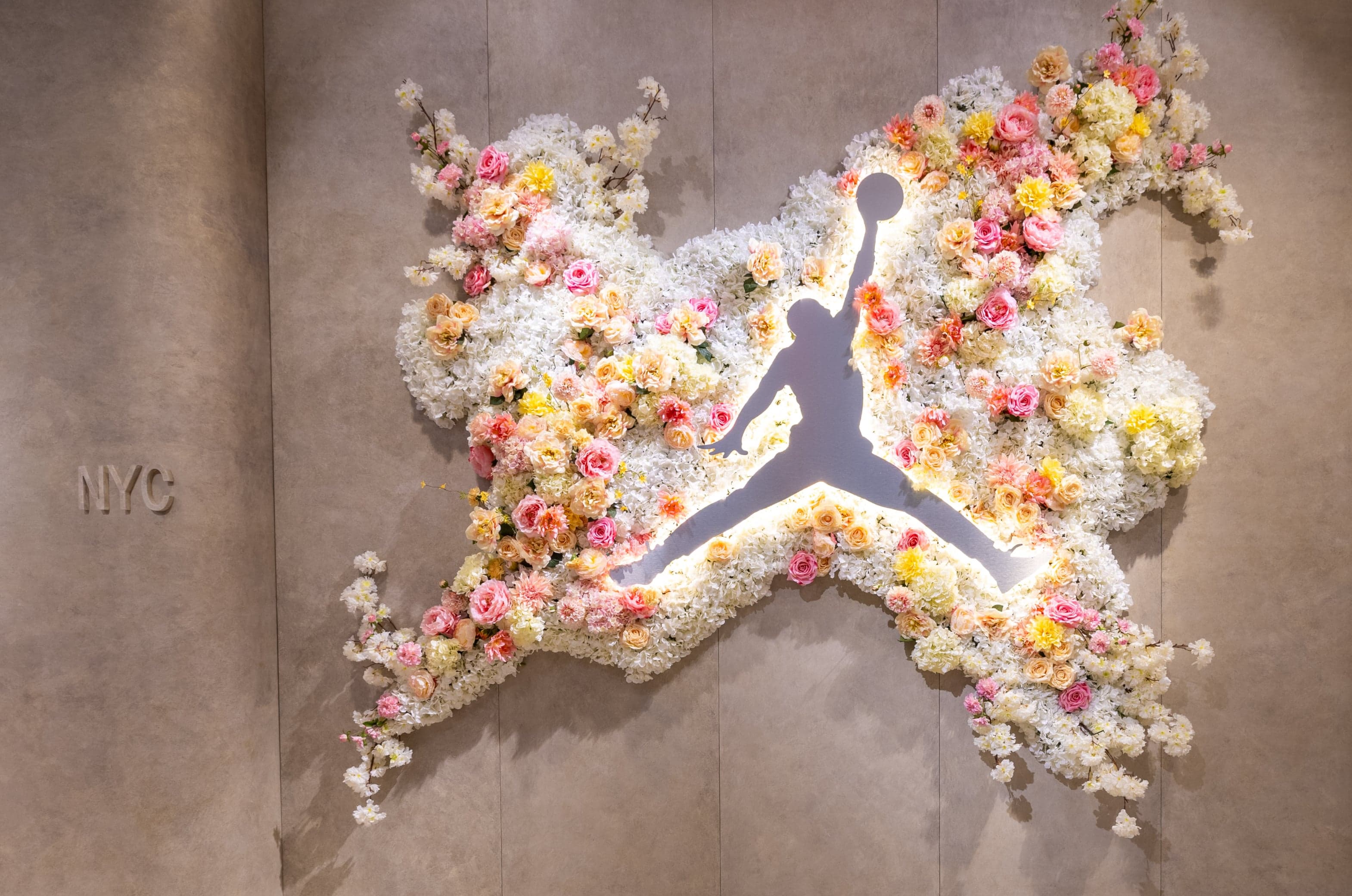 A Jumpman logo set in a burst of pink, peach and white flowers on a stone wall marked NYC