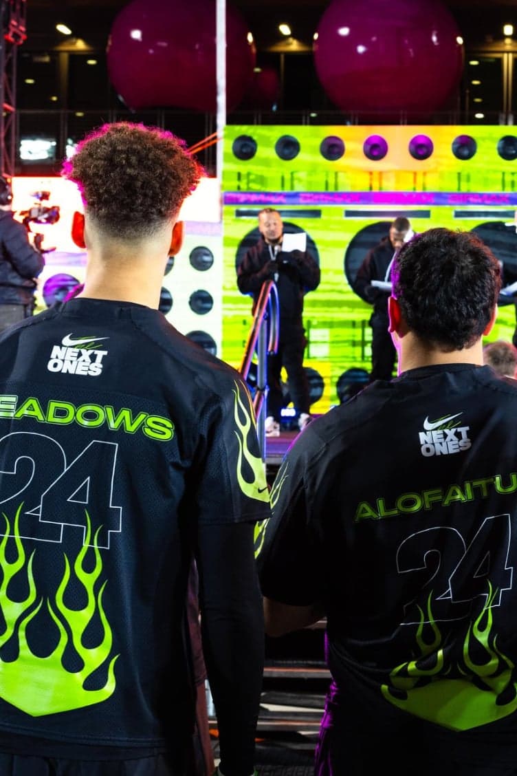 Players from behind in black jerseys with neon flame numbers, facing a stage of speakers