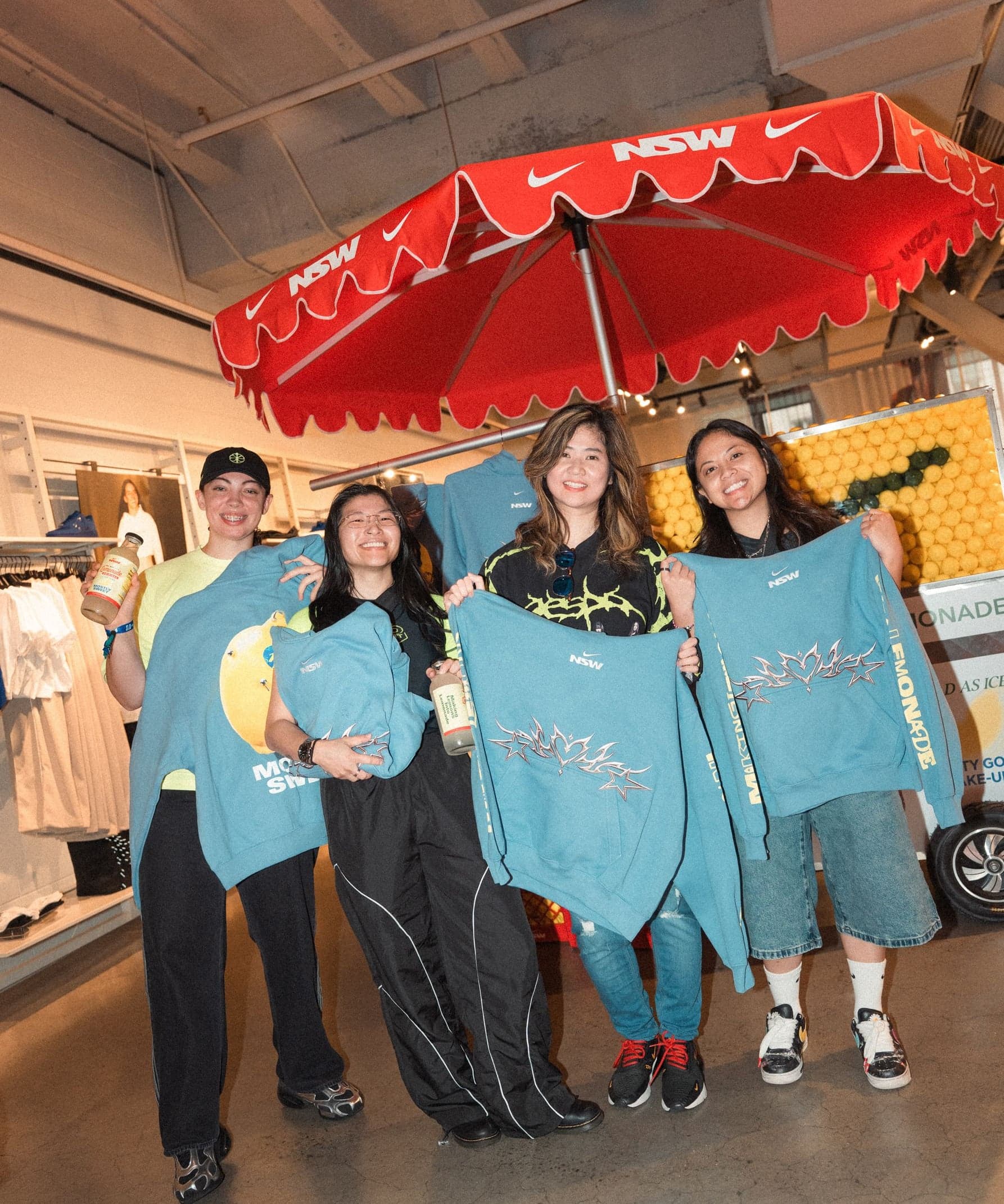 The team in blue hoodies posing with lemons under the lemonade stand umbrella