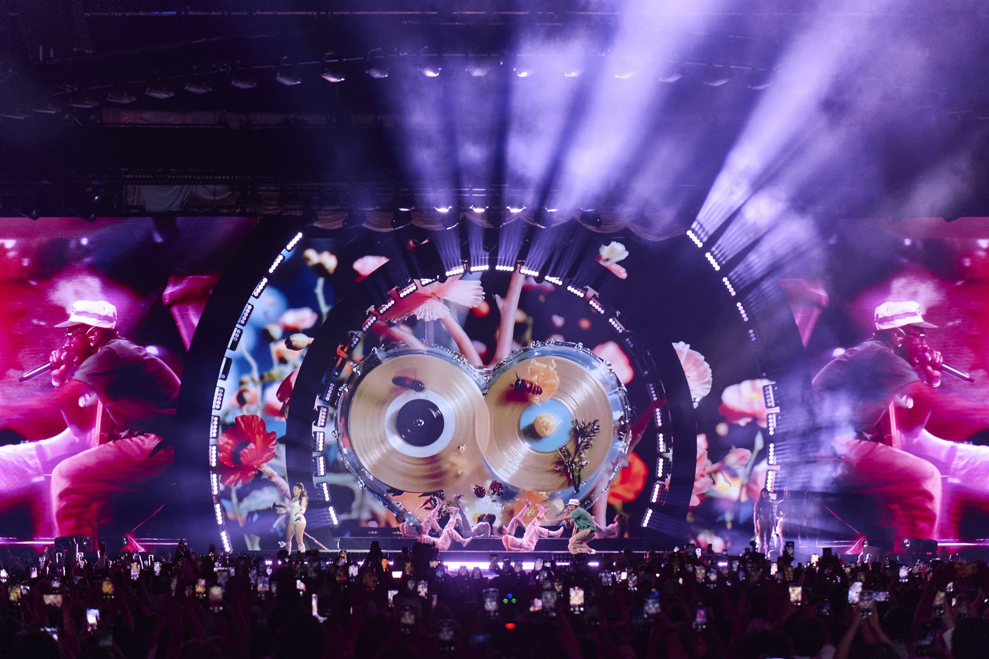 The stage lit purple with two gold discs on the curved LED wall and a crowd in front