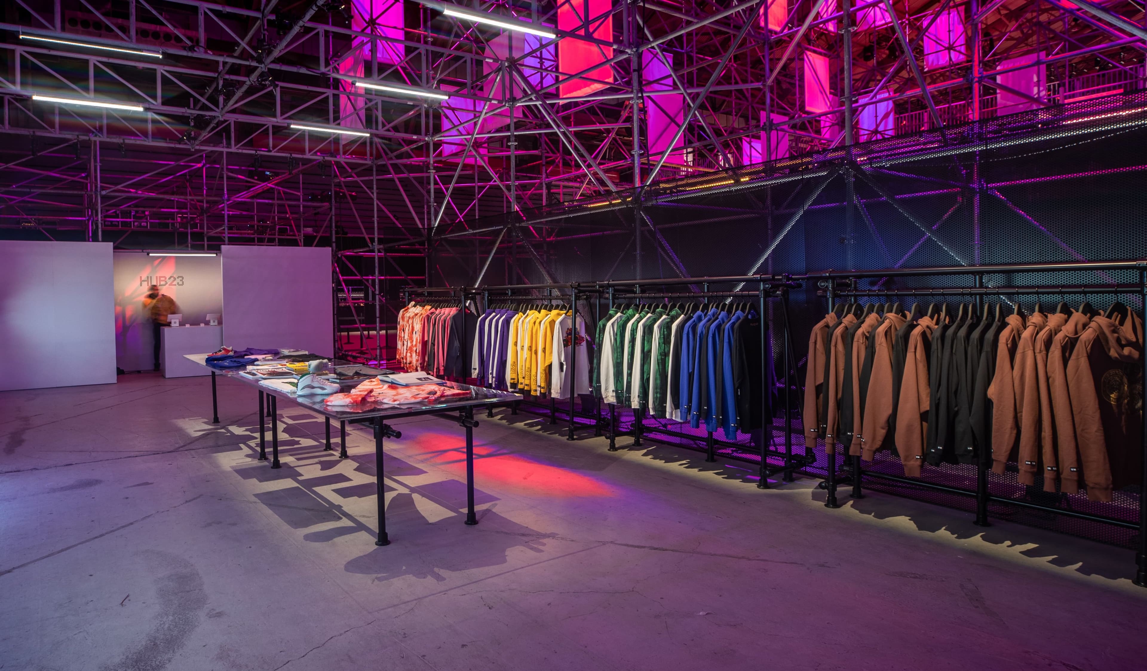 Racks of colourful apparel and display tables under pink-lit scaffolding