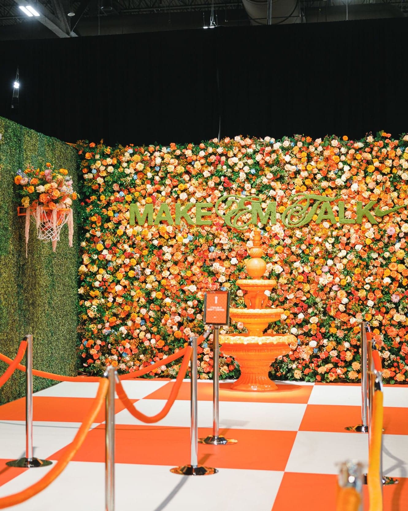 A tiered orange fountain in front of a floral wall, behind orange rope barriers