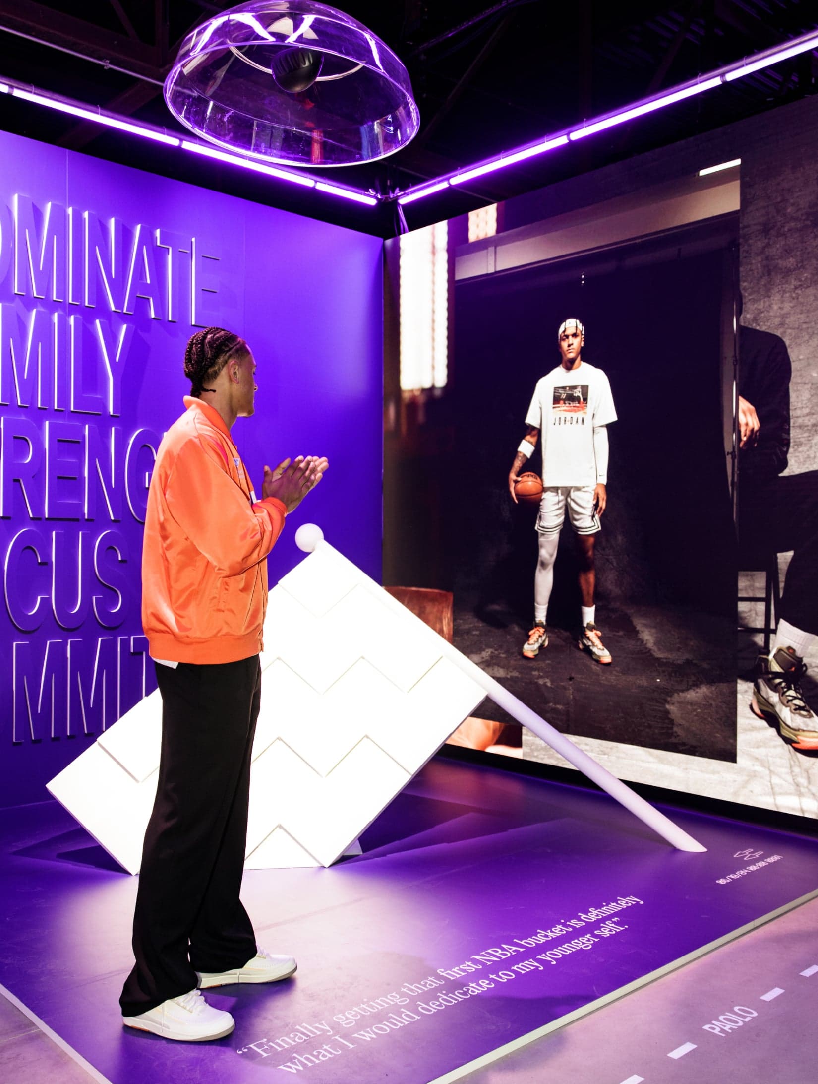 A guest in an orange jacket in a purple player room, looking at a large portrait of a basketball player