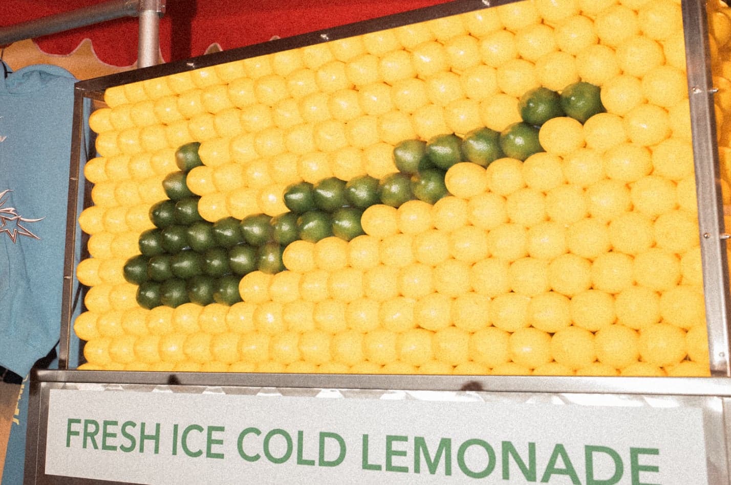 A wall of yellow and green balls forming a Nike swoosh, above a sign reading “Fresh Ice Cold Lemonade”