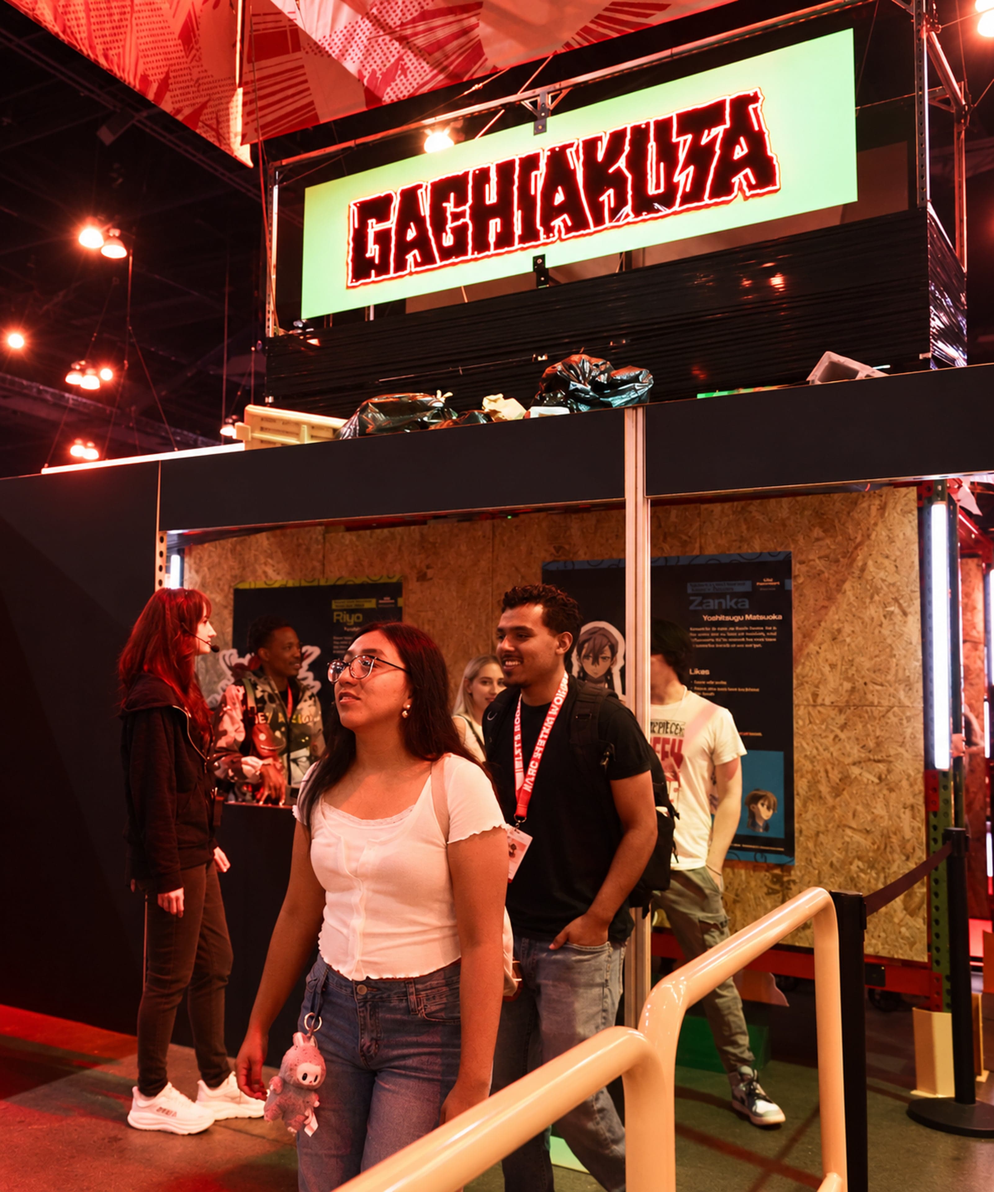 Fans looking up at the trash props beneath the lit Gachiakuta sign