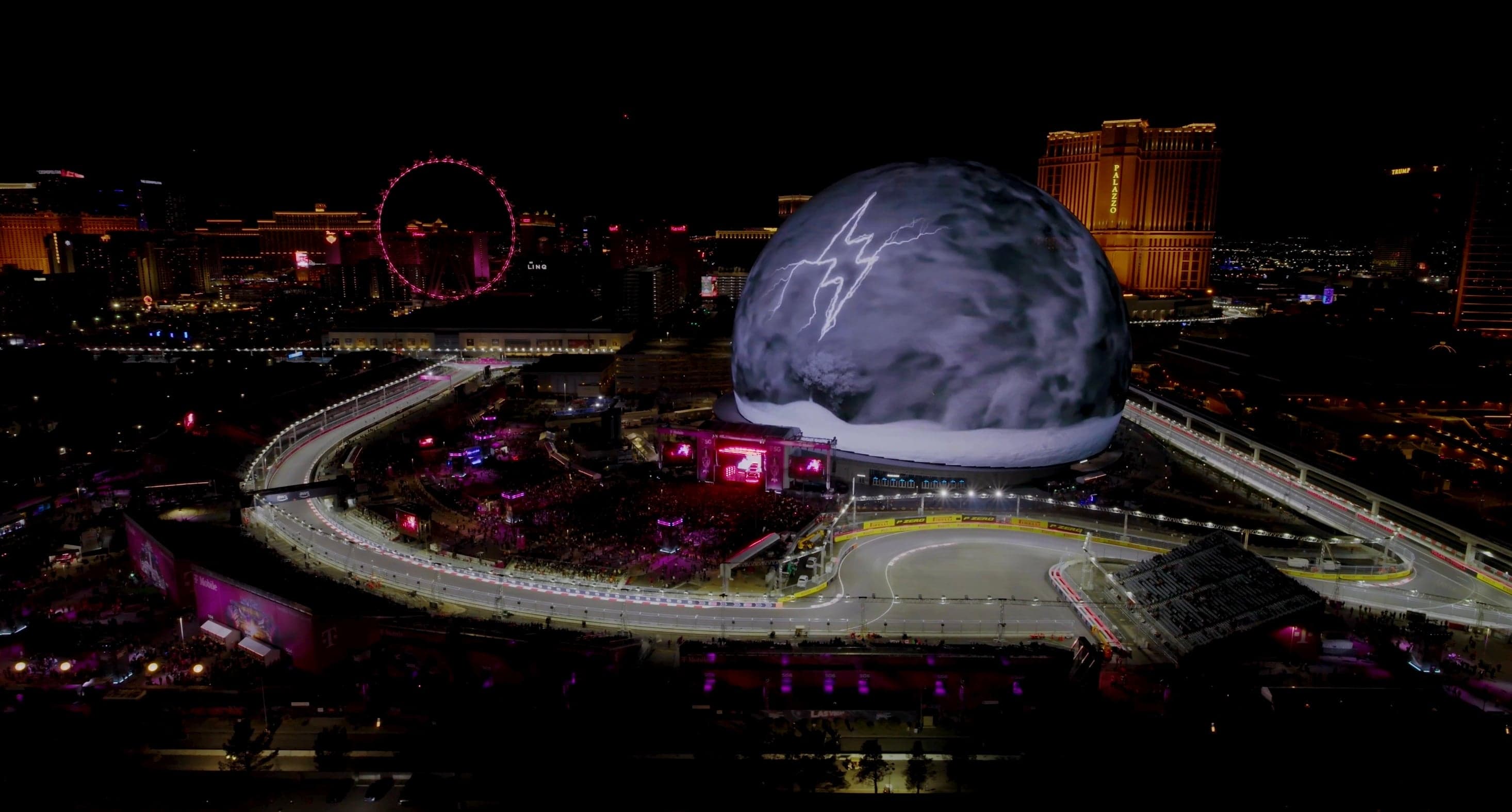 The Sphere covered in grey stone texture beside the lit Grand Prix track at night