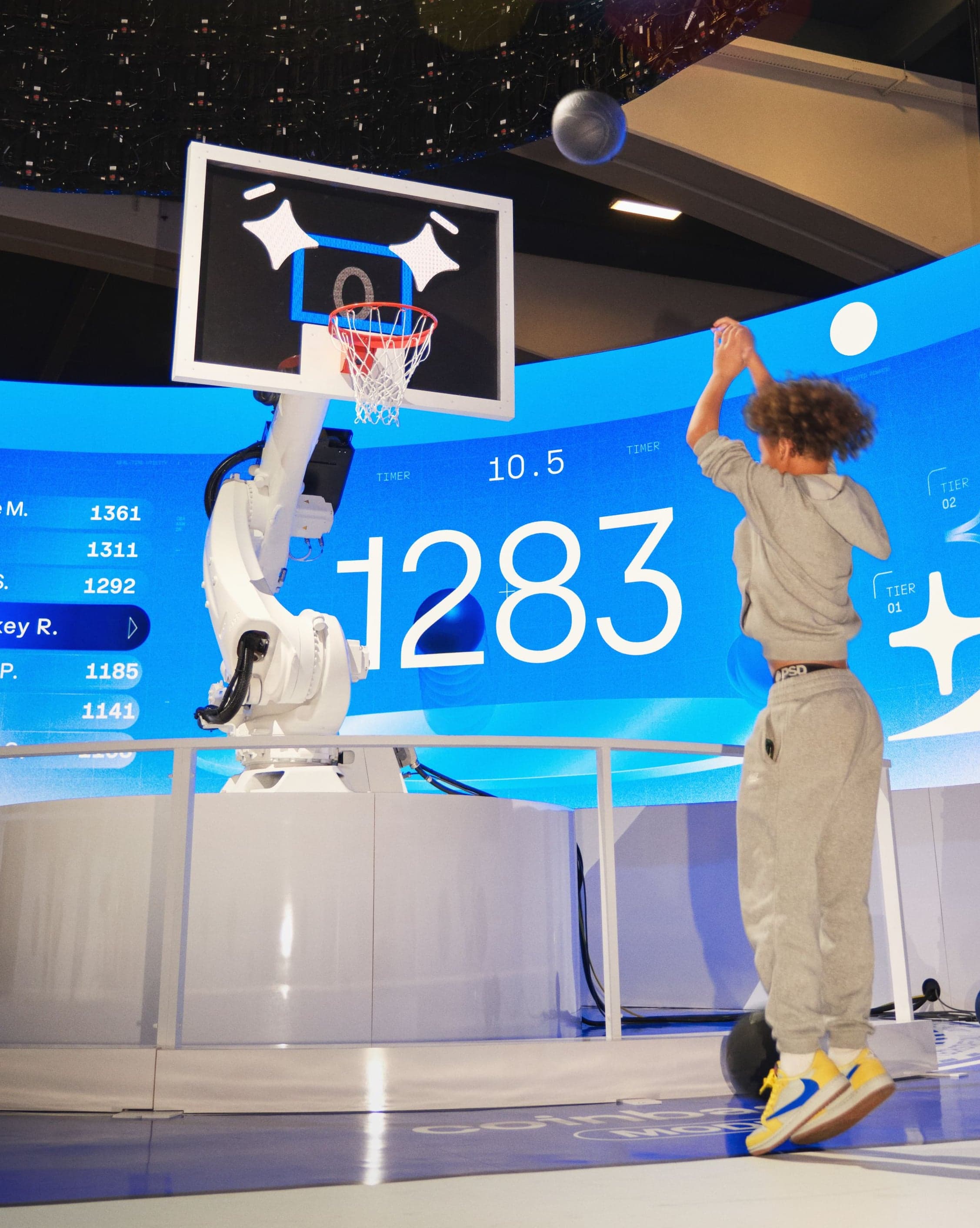 A child jumps to shoot at the robotic hoop as the score display reads 1283